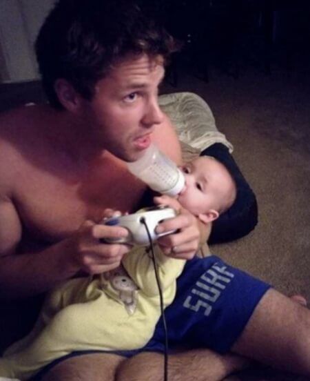 子どもにミルクをあげながら、ゲームに夢中になっている父親